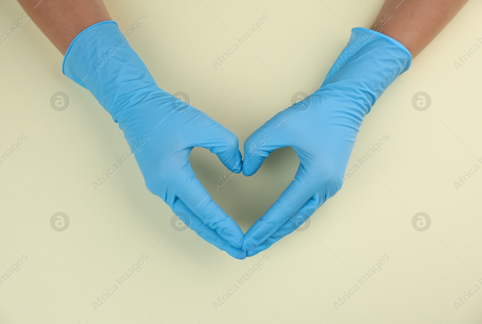 Photo of Person in medical gloves making heart with hands on beige background, top view