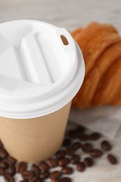 Photo of Coffee to go. Paper cup with tasty drink, croissant and beans on white table, closeup