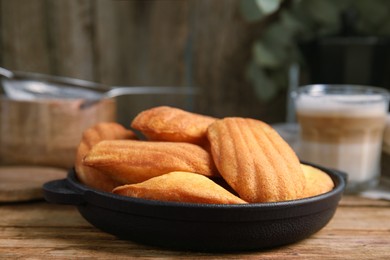 Photo of Delicious madeleine cakes in frying pan wooden table, closeup