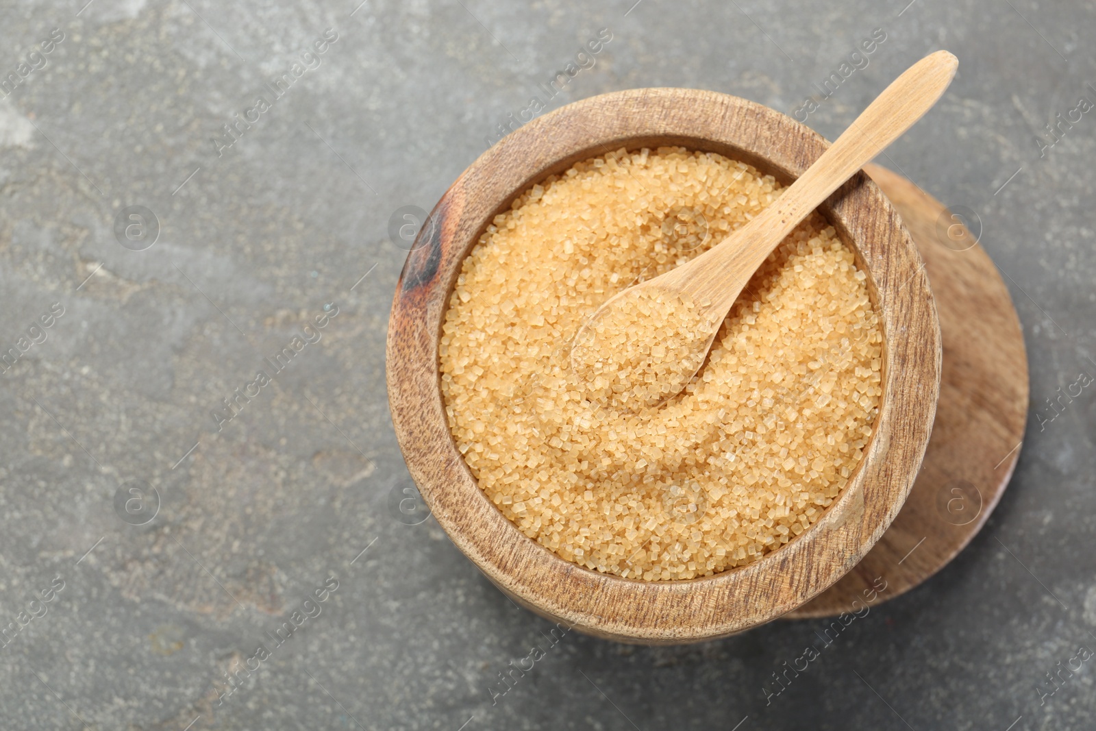 Photo of Brown sugar in bowl and spoon on grey textured table, top view. Space for text