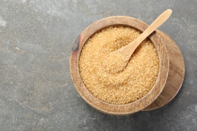 Photo of Brown sugar in bowl and spoon on grey textured table, top view. Space for text