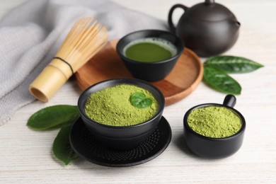 Photo of Green matcha powder, beverage and bamboo whisk on white wooden table