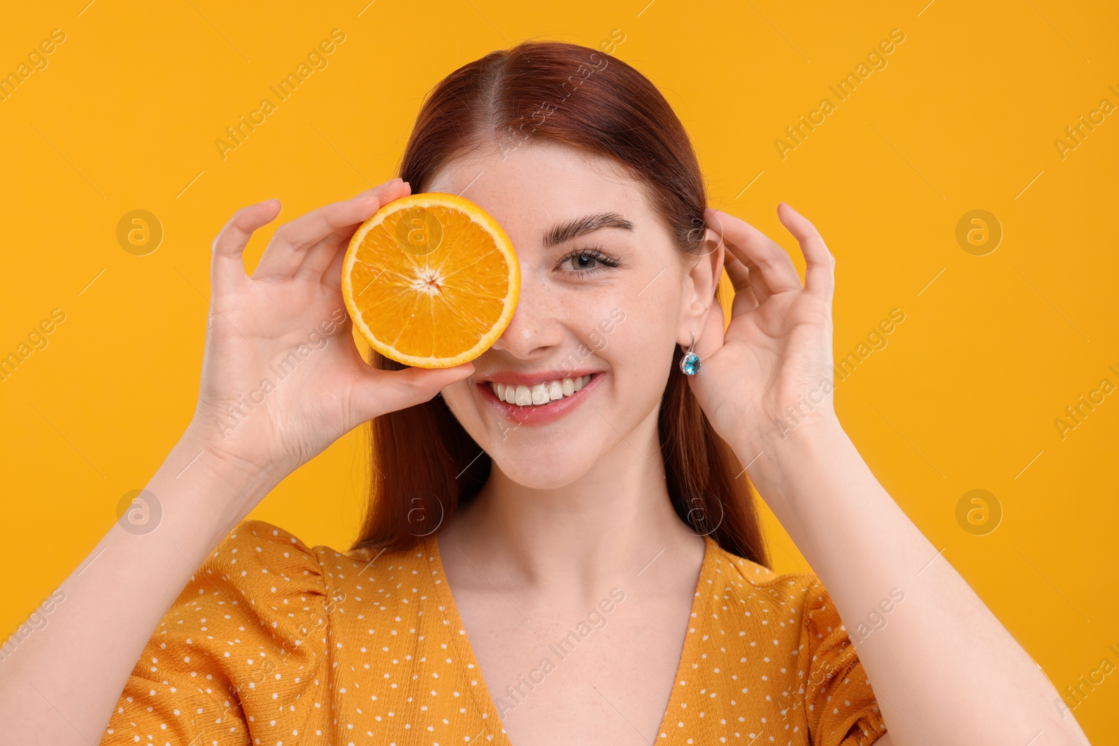 Photo of Smiling woman covering eye with half of orange on yellow background