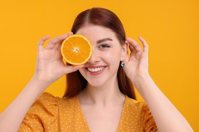 Smiling woman covering eye with half of orange on yellow background