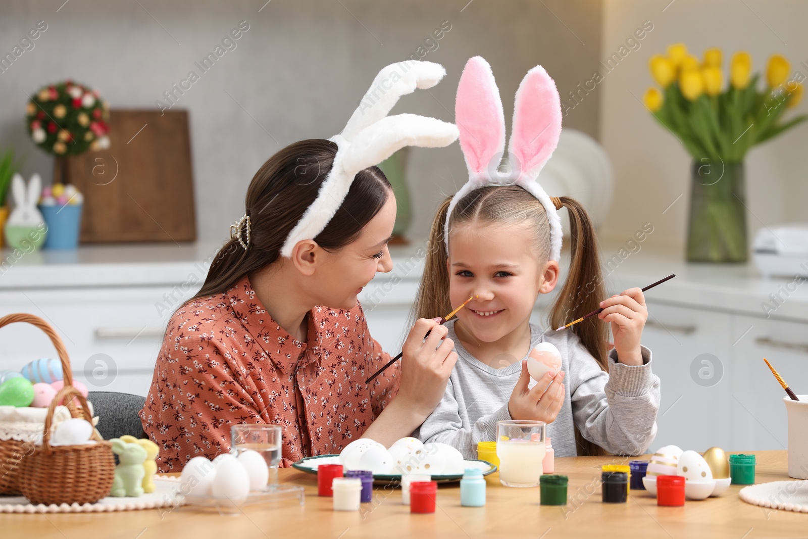 Photo of Mother and her cute daughter painting Easter eggs at table in kitchen