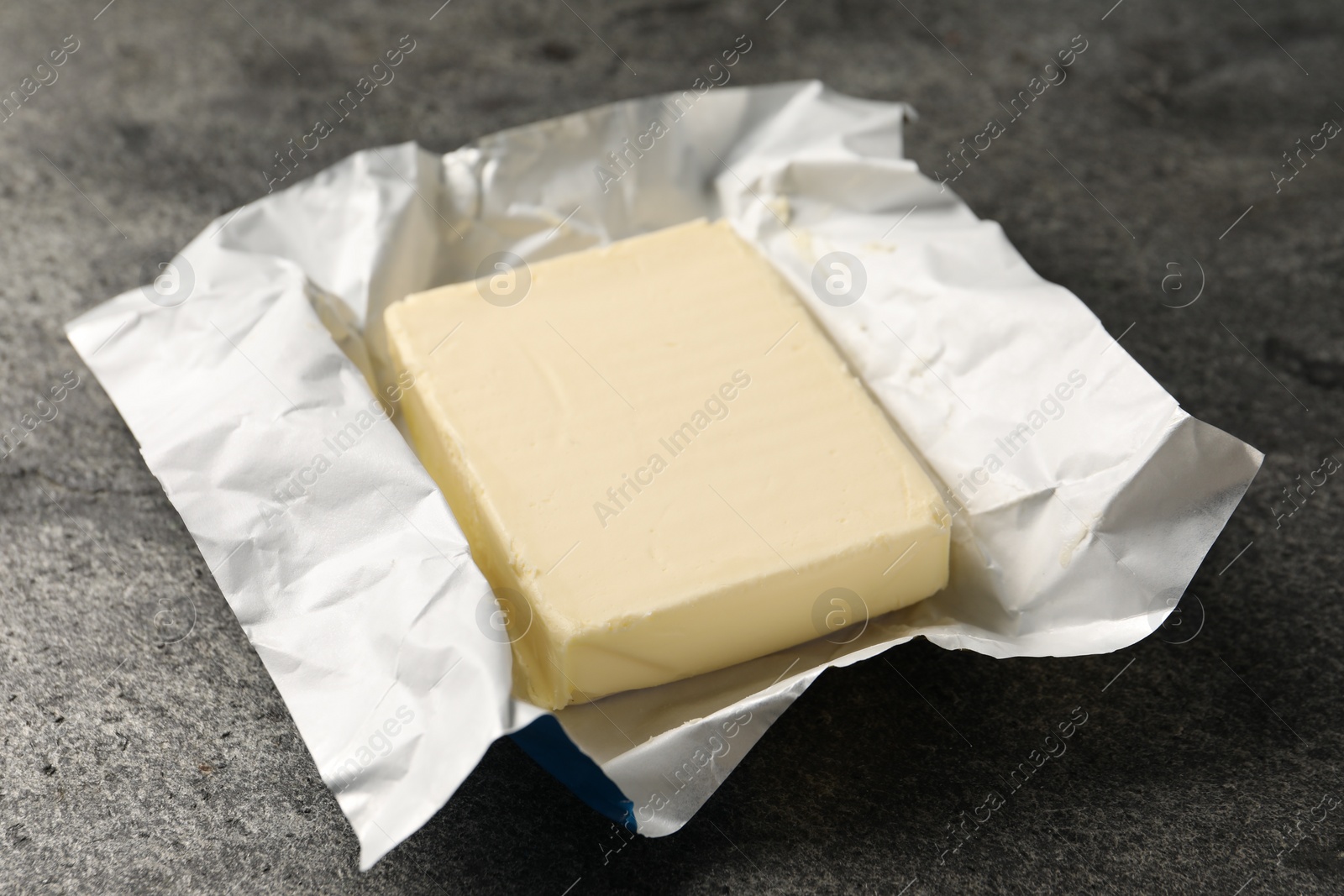 Photo of Block of tasty butter in open foil packaging on grey table, closeup