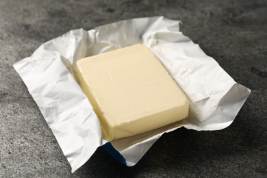 Block of tasty butter in open foil packaging on grey table, closeup