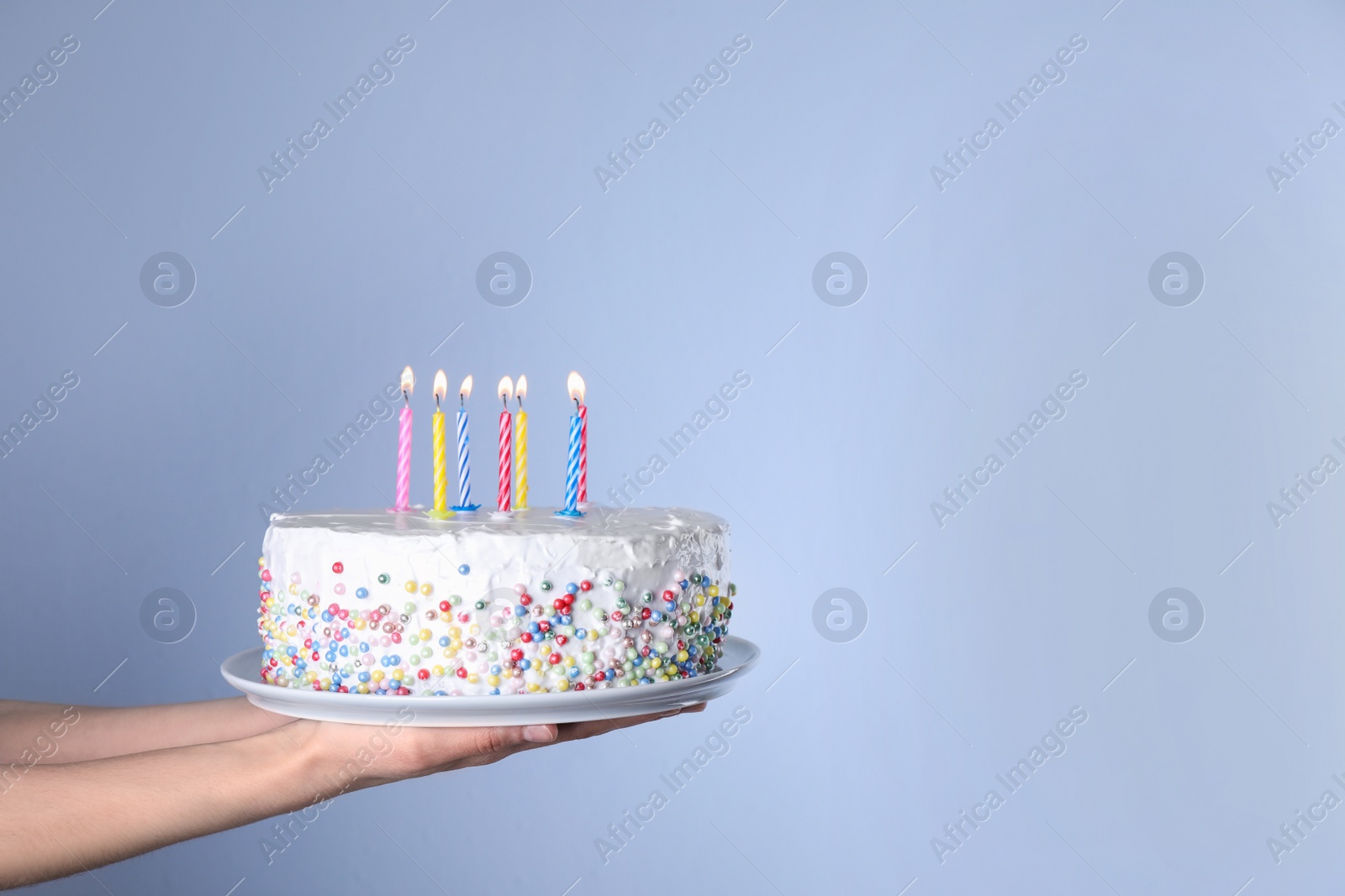 Photo of Woman holding birthday cake with burning candles on light blue background, closeup. Space for text