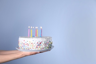 Photo of Woman holding birthday cake with burning candles on light blue background, closeup. Space for text