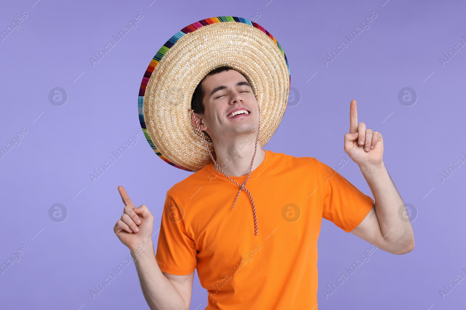 Photo of Young man in Mexican sombrero hat pointing at something on violet background