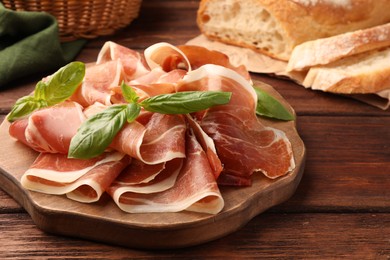 Slices of tasty cured ham and basil on wooden table, closeup