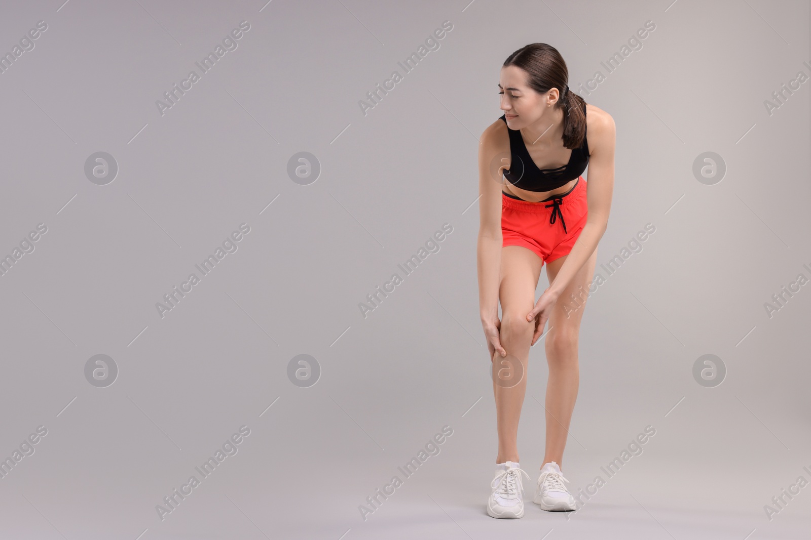 Photo of Young woman suffering from leg pain on grey background, space for text