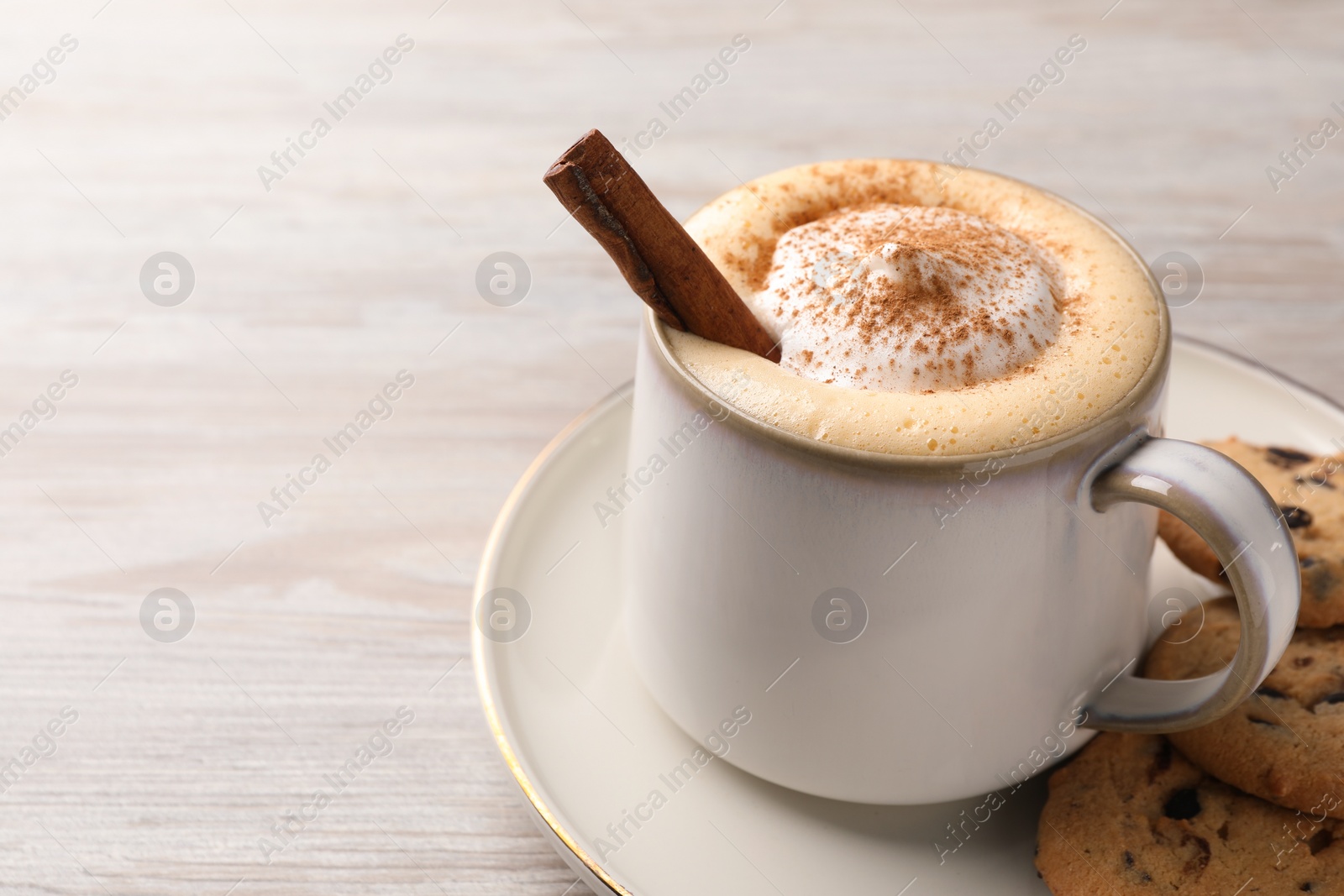 Photo of Cup of delicious eggnog with cinnamon and cookies on wooden table, space for text
