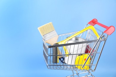 Photo of Small shopping cart with paint and renovation equipment on light blue background. Space for text