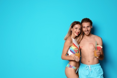 Happy young couple in beachwear with cocktails on color background. Space for text