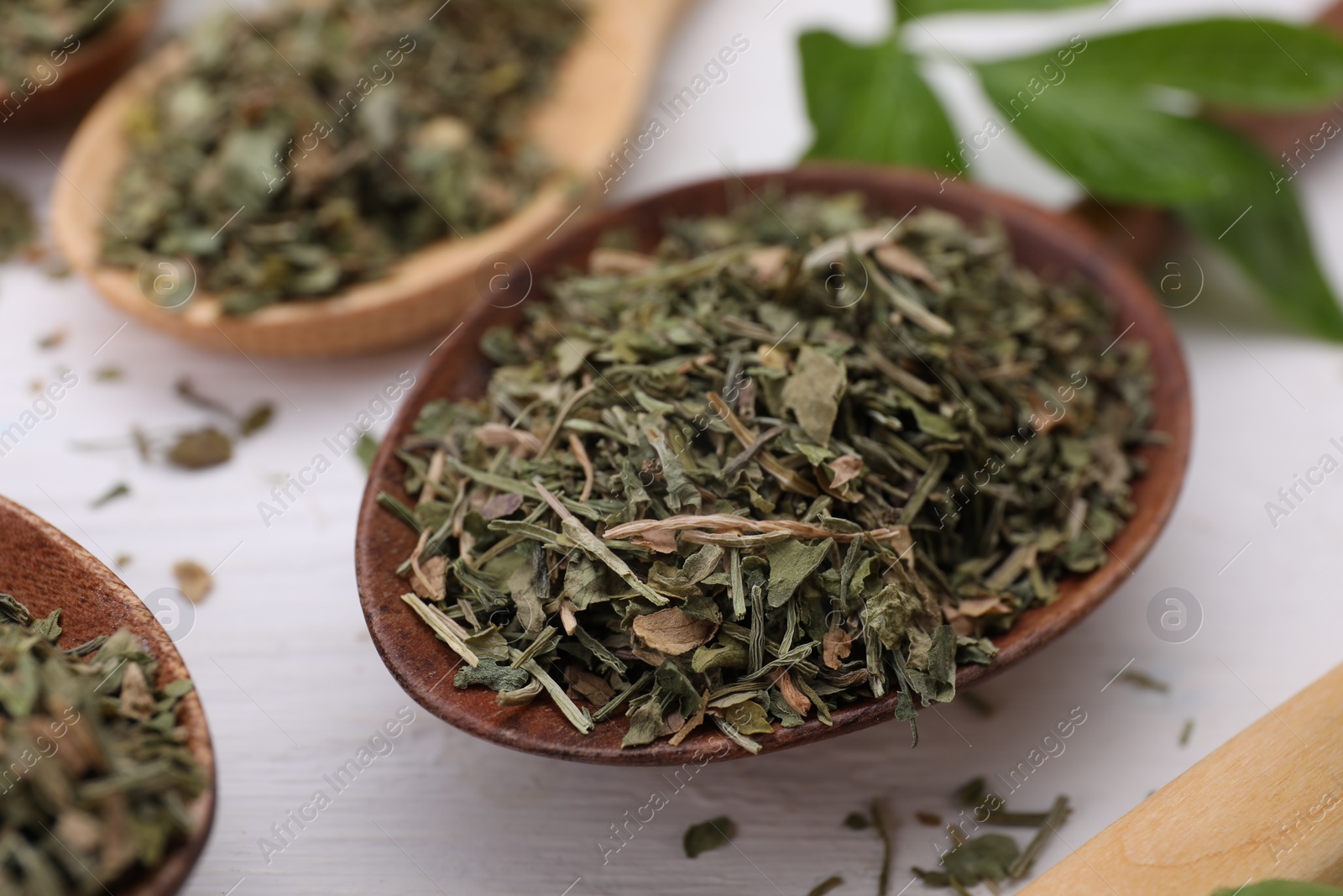 Photo of Spoons with dried aromatic parsley on white wooden table, closeup