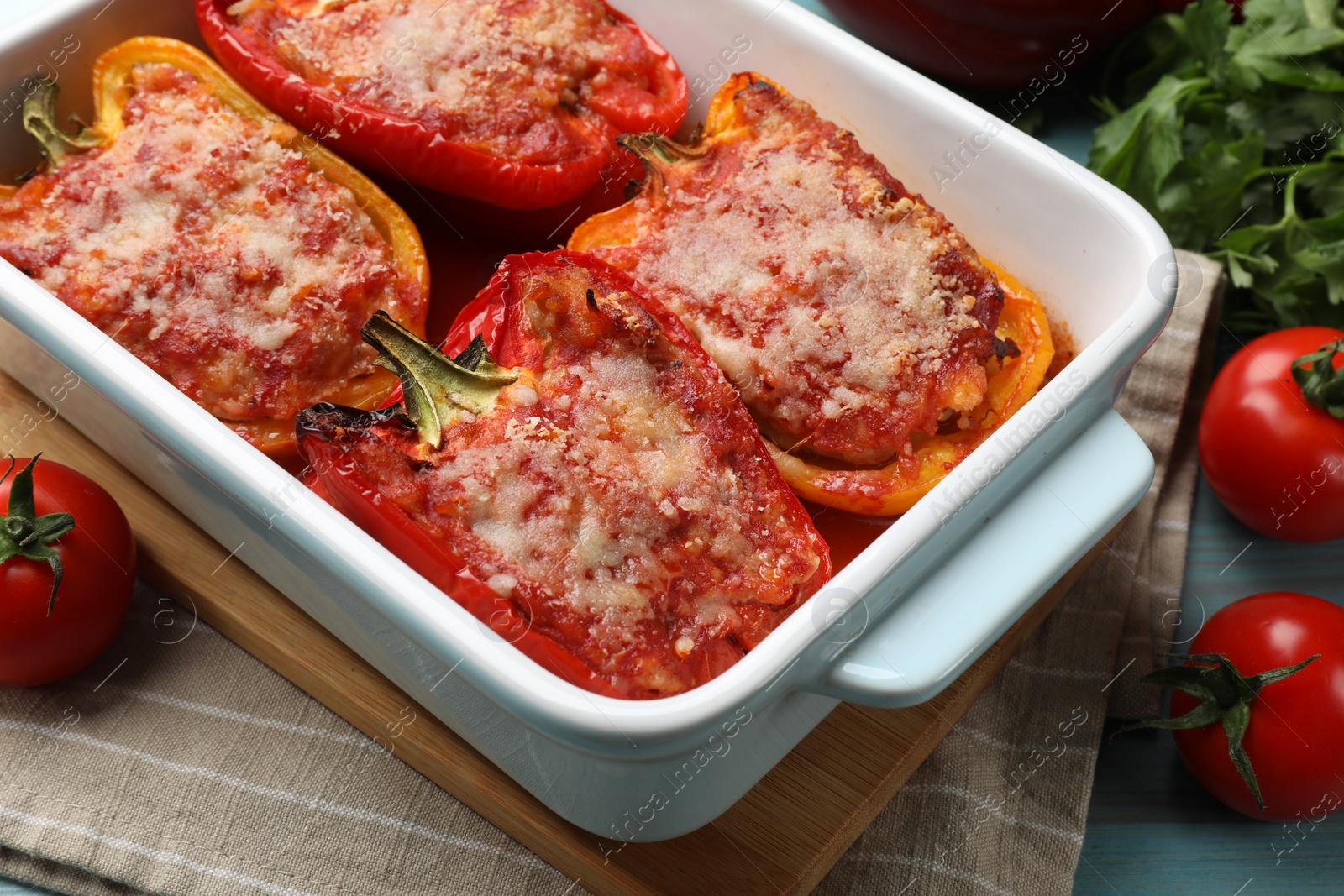 Photo of Tasty stuffed peppers in dish and ingredients on light blue wooden table, closeup