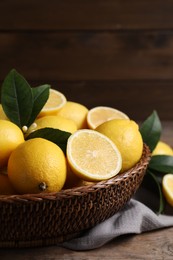 Photo of Many fresh ripe lemons with green leaves on wooden table