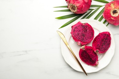 Photo of Plate of delicious red pitahaya fruits with knife on white marble table, flat lay. Space for text