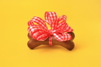 Photo of Bone shaped dog cookie with red bow on yellow background, closeup