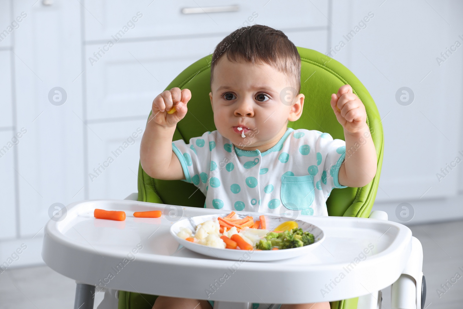 Photo of Cute little baby eating healthy food in high chair at home