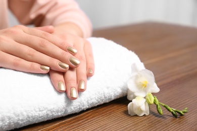 Woman with gold manicure on rolled towel at table, closeup. Nail polish trends