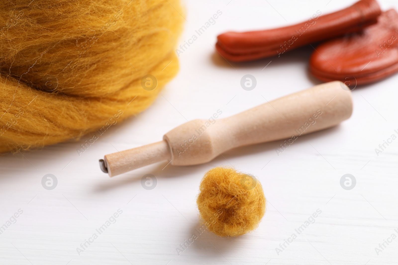 Photo of Orange woolen ball and needle felting tools on white wooden table, closeup