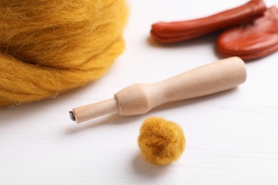 Orange woolen ball and needle felting tools on white wooden table, closeup