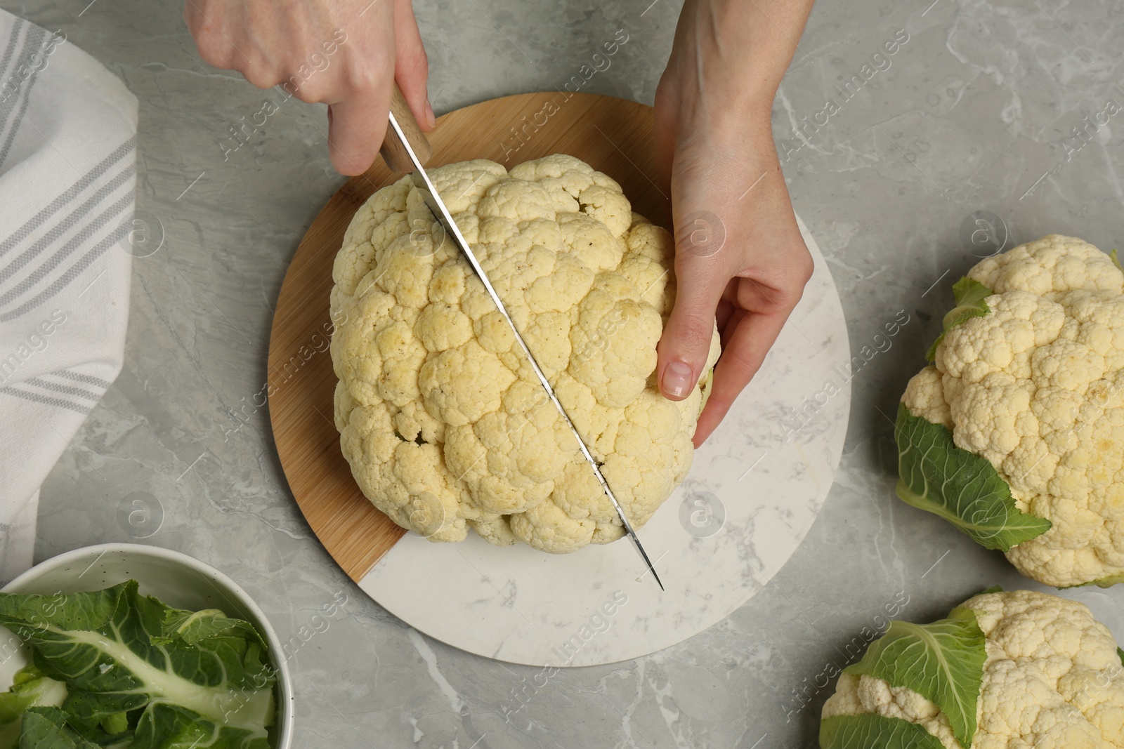 Photo of Woman cutting fresh cauliflower at light grey table, top view
