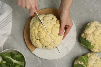 Photo of Woman cutting fresh cauliflower at light grey table, top view