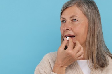 Photo of Senior woman taking pill on light blue background. Space for text