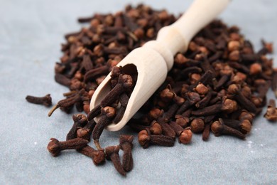 Pile of aromatic dried clove buds and scoop on grey table, closeup