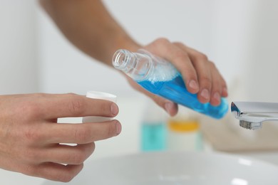 Photo of Young man using mouthwash in bathroom, closeup