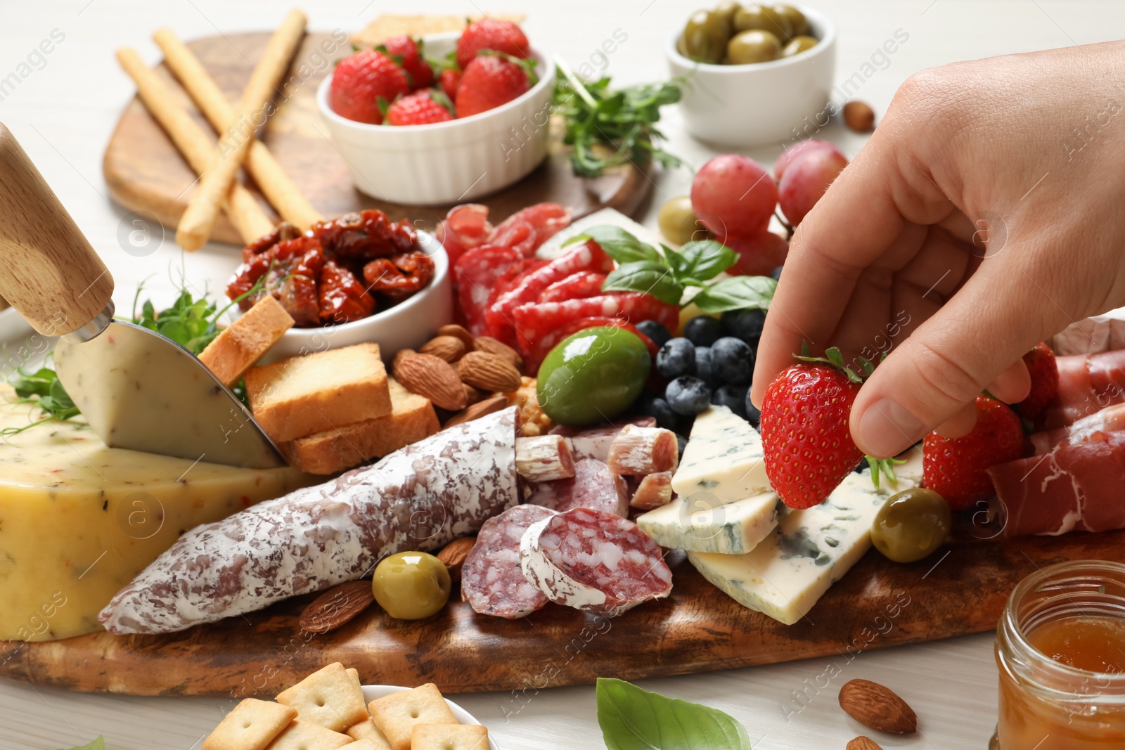 Photo of Woman taking strawberry from board with different appetizers at white wooden table, closeup