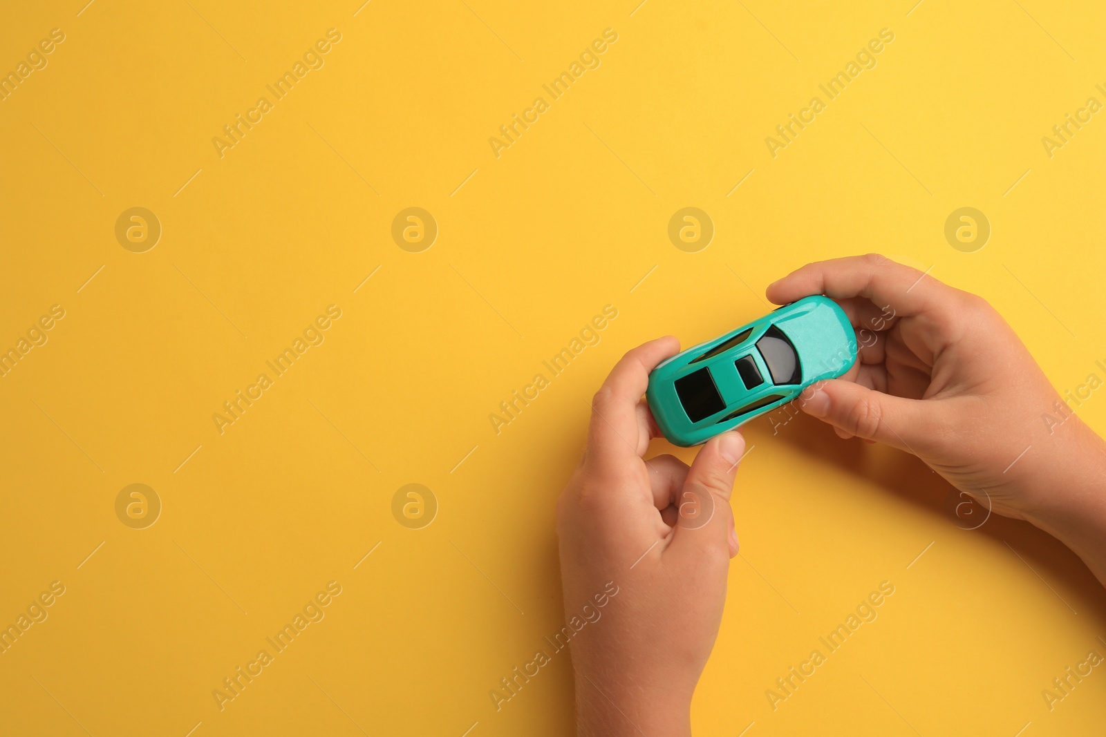 Photo of Child playing with toy car on yellow background, top view. Space for text