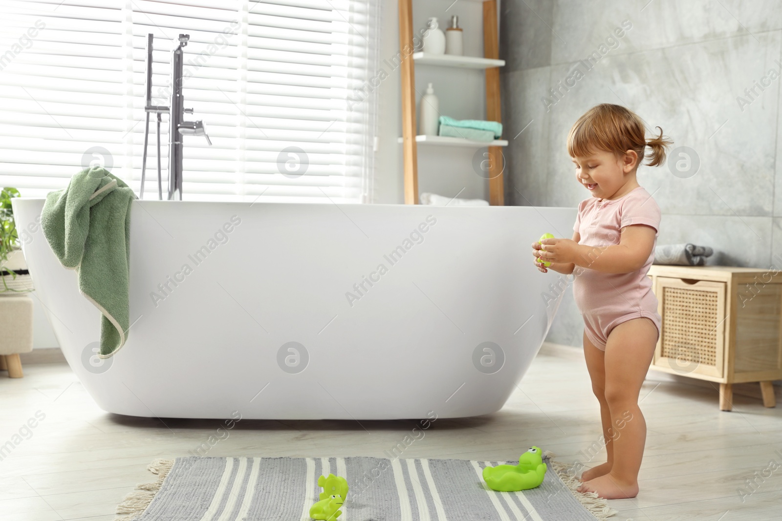 Photo of Cute little girl with toys in bathroom