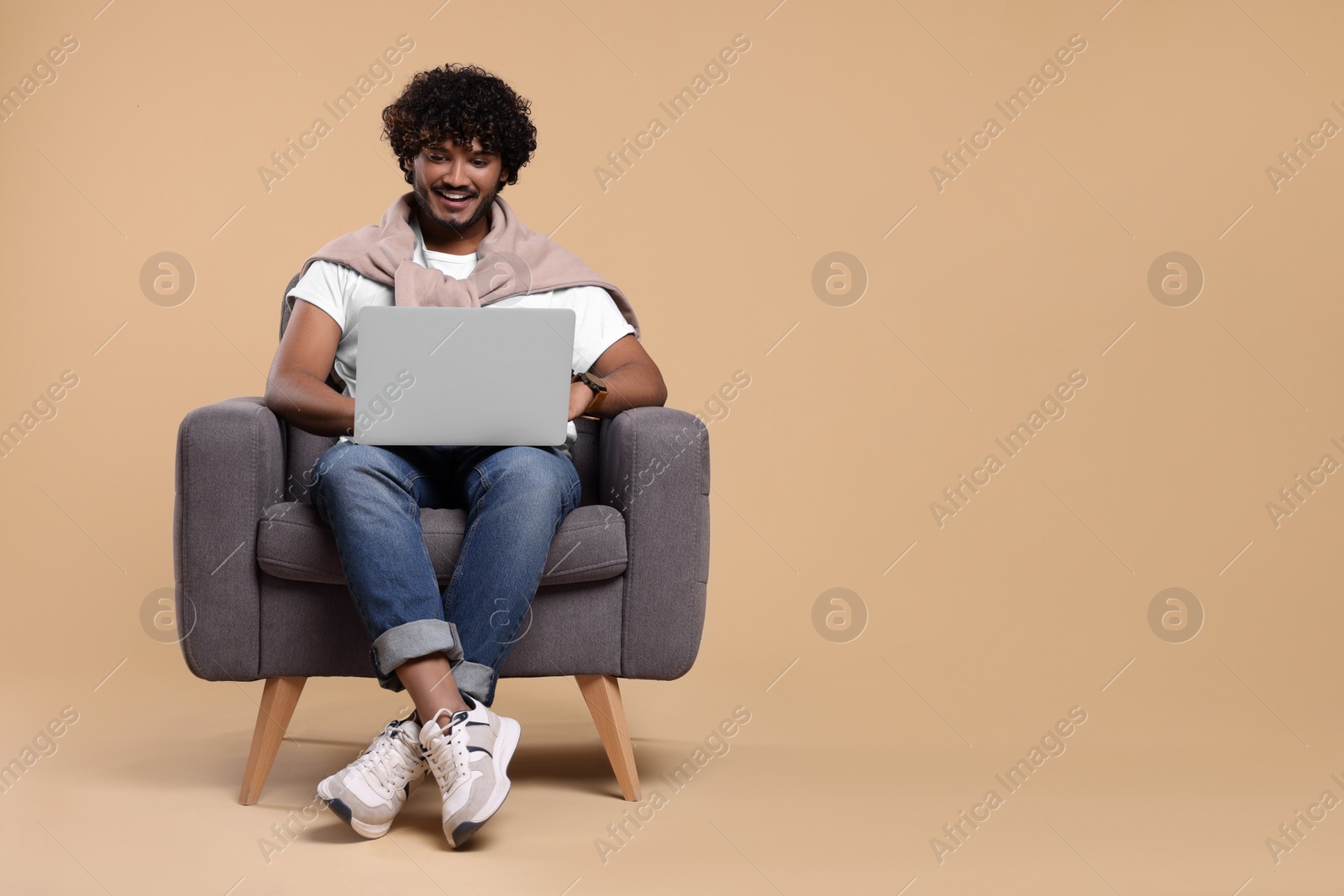 Photo of Smiling man with laptop sitting in armchair on beige background. Space for text