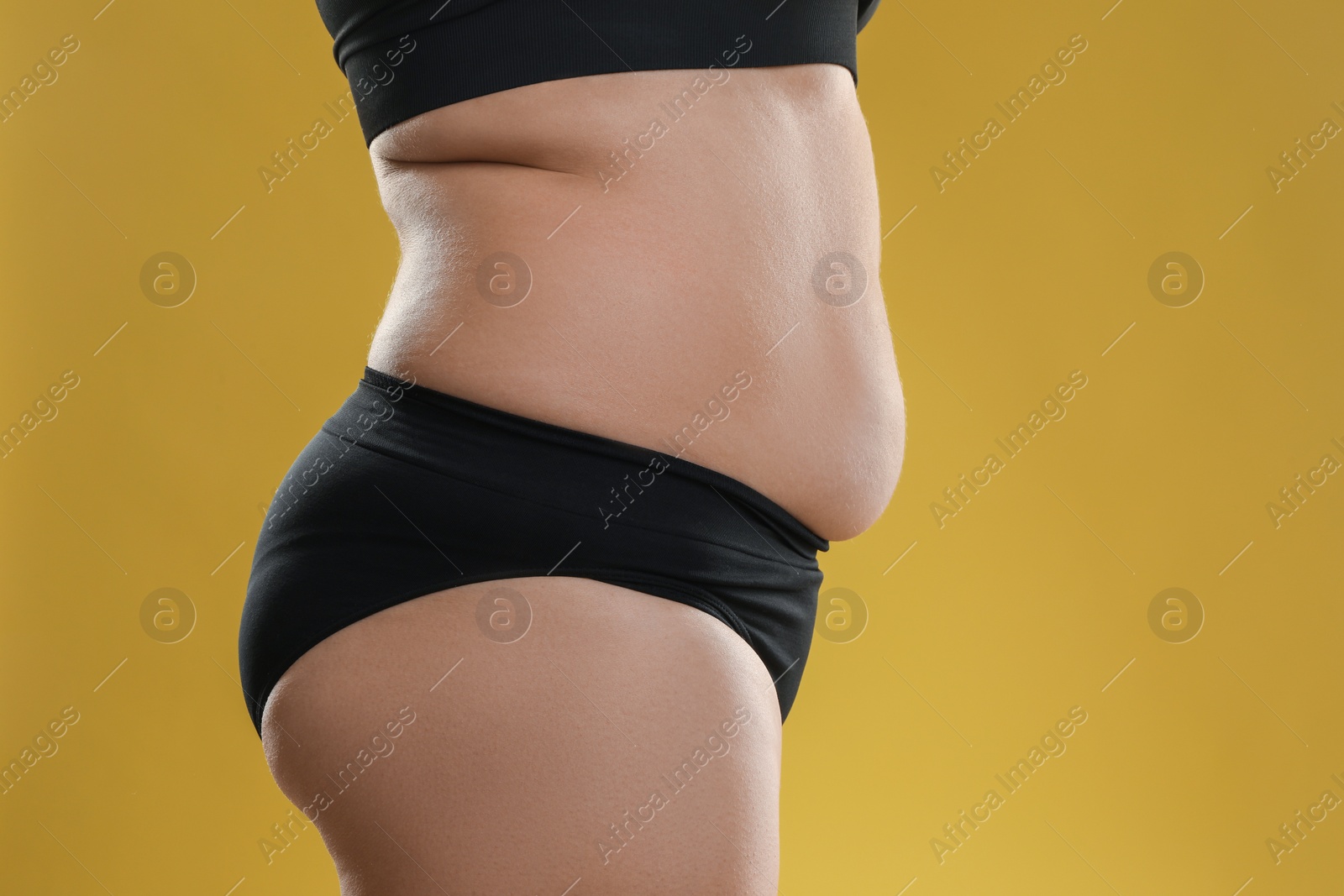 Photo of Woman with excessive belly fat on goldenrod background, closeup. Overweight problem