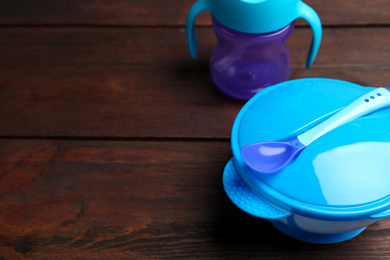 Plastic dishware on wooden table, space for text. Serving baby food