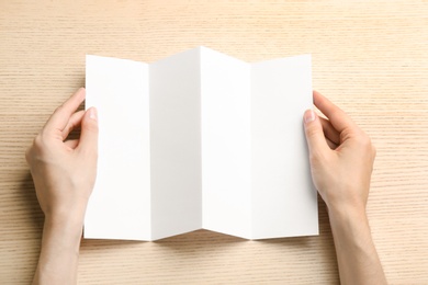 Photo of Young woman holding blank brochure at light wooden table, top view. Mock up for design