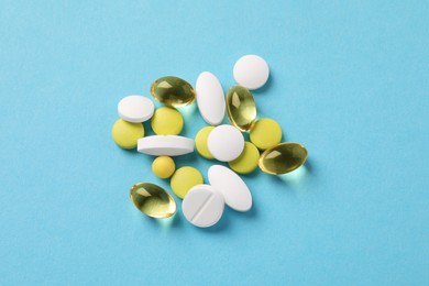 Pile of different pills on light blue background, flat lay