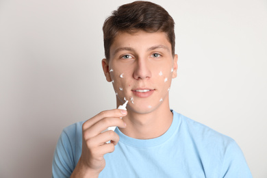 Photo of Teen guy with acne problem applying cream on light background