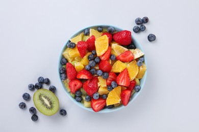 Yummy fruit salad in bowl and ingredients on light grey background, flat lay
