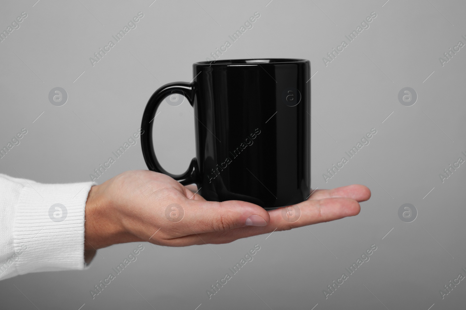 Photo of Man holding black mug on gray background, closeup