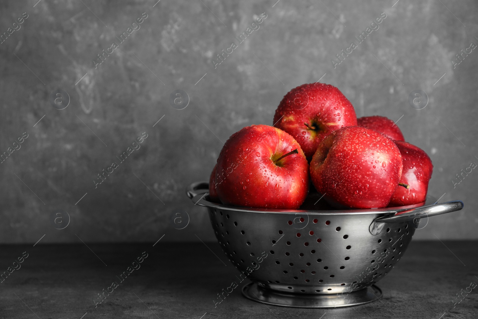 Photo of Juicy red apples in colander on table. Space for text