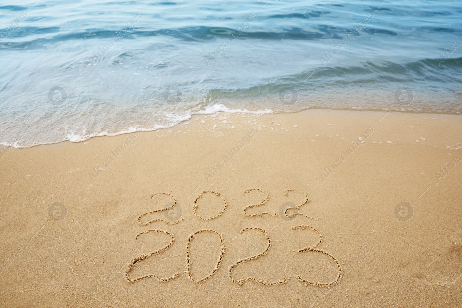 Photo of Dates written on sandy beach. 2022 washed by sea wave as New 2023 Year coming