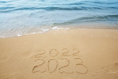 Dates written on sandy beach. 2022 washed by sea wave as New 2023 Year coming