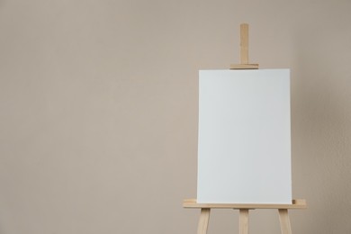 Wooden easel with blank canvas on beige background. Space for text