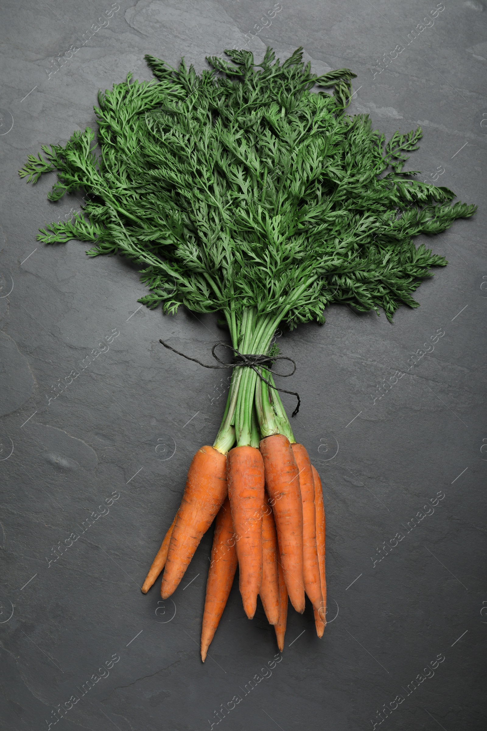 Photo of Bunch of tasty raw carrots on black slate table, top view