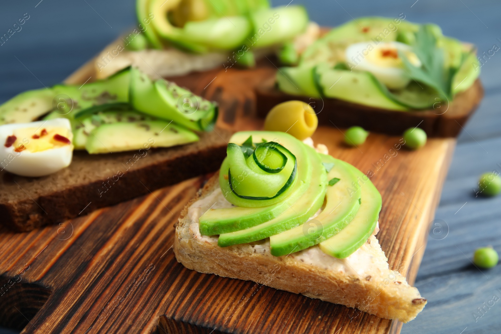 Photo of Crisp toasts with sliced avocado and cream cheese on wooden board, closeup